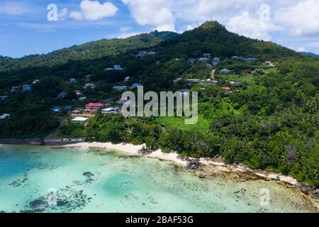 Aus der Vogelperspektive auf den üppigen grünen Berg mit verstreuten Dorfhäusern und den Anse Royale Strand darunter, Mahe Island, Seychellen Stockfoto