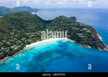 Blick von der Drohne auf den Strand von Anse Petite mit Häusern am Hügel, türkisfarbene Bucht und tropische Küste, Mahe, Seychellen Stockfoto