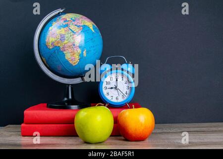 Der Globus und die blaue Uhr stehen auf einem Stapel Bücher, neben einem apfel Stockfoto