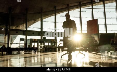 Silhouette der Frau stackte am Flughafenterminal über die Flugannullierung, rief Familie an und saß wegen Coronavirus in einem fast leeren Flughafenterminal Stockfoto