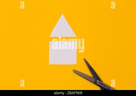 Schere und Haus auf dem gelben Hintergrund Papier geschnitten Stockfoto