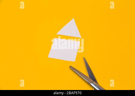 Schere und Haus auf dem gelben Hintergrund Papier geschnitten Stockfoto