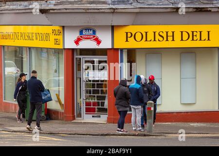 Clydebank, Großbritannien. März 2020. Kunden stehen außerhalb eines lokalen Shops, während sie warten, nacheinander eingelassen zu werden, wobei einige die soziale Distanzierung respektieren. Kredit: Colin Poultney/Alamy Live News Stockfoto