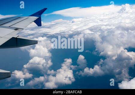 Blick aus dem Fenster des Flugzeugflügels unter dem Sonnenlicht umgeben von Wolken am Tag Stockfoto