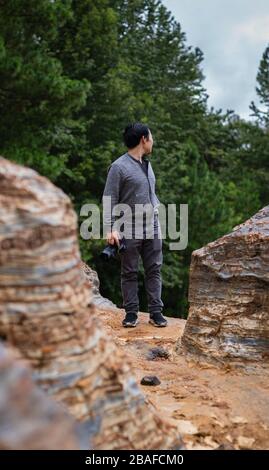 Vertikale Aufnahme einer Person, die auf einer Klippe steht und hält Eine Kamera und ein Blick nach hinten Stockfoto