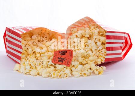 Horizontaler Schuss von zwei Säcken Popcorn, die aufeinander liegen und den Popcorn in beiden Fällen mit zwei Kinokarten auf dem Popcorn verschütten. Weißer Rücken Stockfoto