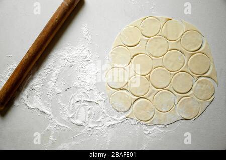 Roher ausgerollter Teig, der in Runden mit Mehl auf dem Weißen Tisch geschnitten wurde. Verarbeiten Sie Gardudeln. Stockfoto