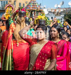 Hindu-Frauen in Saris, lächelnd, während sie an einer Prozession und Feier des Chariot-Festivals teilnehmen und Angebote auf dem Kopf, London, Großbritannien, tragen Stockfoto