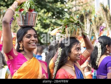 Junge Hindu-Frauen in Saris, die lächeln, während sie an einer Festprozession und Feier des Chariot-Festivals teilnehmen und Opfergaben auf dem Kopf tragen Stockfoto