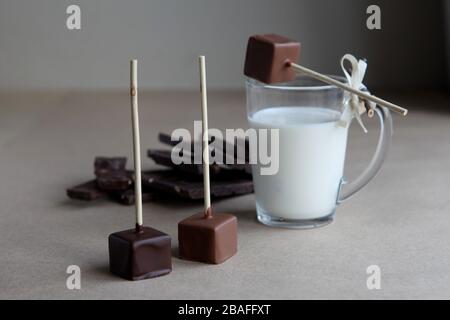 Schokoladenwürfel auf einem Stock mit Milchbecher und aromatischem Kakao und Schokolade auf braunem Grund. Heißer Kakao mit Milch in transparentem Glasbecher, gebrochen Stockfoto