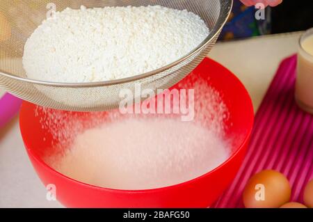 Backzutaten und Utensilien zum Kochen von Schwammkuchen. Backen Des Schwammkochs Verarbeiten. Frau siebt das Mehl durch eine Sieve. Stockfoto