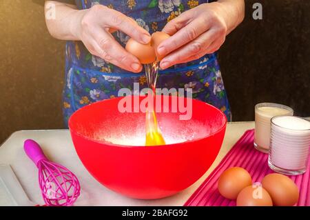 Backzutaten und Utensilien zum Kochen von Schwammkuchen. Backen Des Schwammkochs Verarbeiten. Frau bricht ein Ei im Teig. Stockfoto