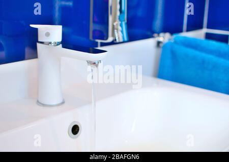 Weißer Waschtisch in der Nähe mit fließendem Wasser im Badezimmer mit blauen Kacheln. Stockfoto