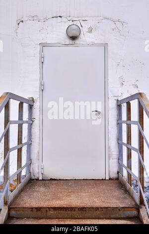 Graue Metalltür mit eisernem Vorbau in einer rissigen weißen Wand Stockfoto