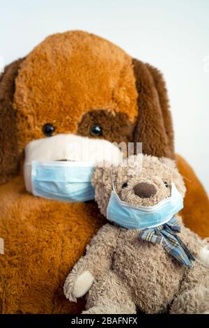 Zwei braune Teddybären - klein und groß - tragen aus gesunden Gründen blaue Schutzmasken Stockfoto