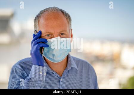 Ein Mann, der Schutzmasken und blaue Latexhandschuhe verwendet, während er das Handy in der urbanen Umgebung verwendet Stockfoto