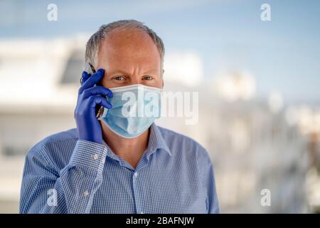 Ein Mann, der Schutzmasken und blaue Latexhandschuhe verwendet, während er das Handy in der urbanen Umgebung verwendet Stockfoto