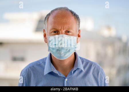 Porträt eines ernsthaften Mannes, der in urbaner Landschaft eine blaue medizinische Schutzmaske trägt Stockfoto