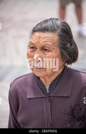 Shanghai, China - 4. Mai 2010: Nahaufnahme des Gesichts der älteren, grauenden, in violettem Gewand gekleideten Seniorin. Stockfoto