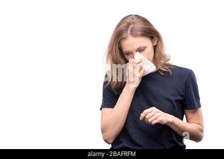 Kranke junge Frau mit Rhinitis, die Taschentuch hält, indem sie die Nase weht, während sie vor der Kamera über weißem Hintergrund steht Stockfoto