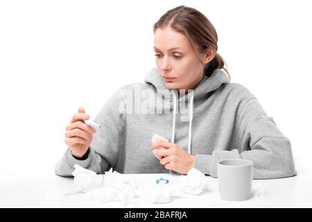 Junge kranke Frau, die während der Selbstisolation während der Kovid19-Spreizung Thermometer beim Messen der Temperatur betrachtet Stockfoto