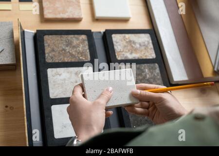 Die Hände junger Designerinnen, die die Probe der Platte über dem Arbeitsplatz halten, während sie ihre Eigenschaften erlernen und eine für neue Bestellungen auswählen Stockfoto