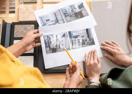 Die Hände junger Innenarchitekten, die Fotografien moderner Räume durchschauen, während sie über ihren Stil sprechen und einen davon auswählen Stockfoto