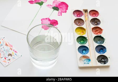 Aquarellgemälde mit rosafarbenen magnolienblüten und künstlerischen Werkzeugen auf weißem Tisch. Stillleben Komposition von künstlerischen Arbeitsplätzen Stockfoto