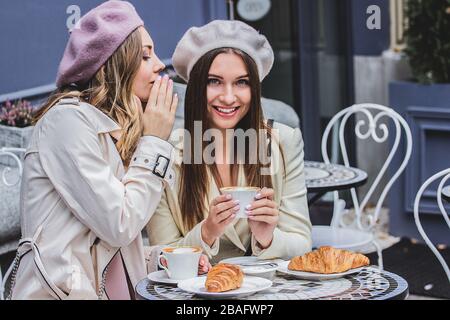 Geheimnisse mit besten Freunden teilen. Hochwinkeliger Blick auf die schöne Frau in Beret, die ihrem Freund beim Kaffeetrinken im französischen Café flüstert. Frauen fr Stockfoto