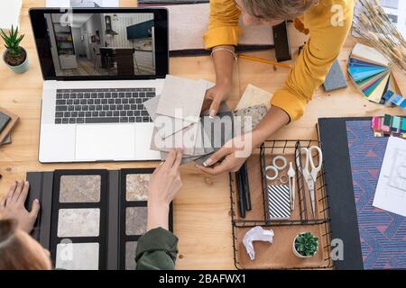 Zwei junge Innenarchitekten besprachen Muster von Platten nach Arbeitsplatz und wählten eine für Wände im Raum auf einem Laptop-Display Stockfoto