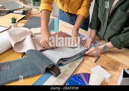 Hände von zwei Innenarchitekten, die am Schreibtisch stehen und Stoffmuster für einen der neuen Aufträge auswählen, während sie im Studio arbeiten Stockfoto