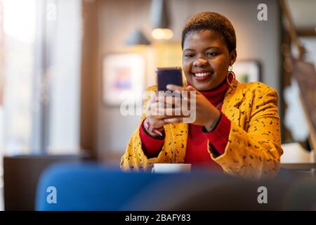 Fröhliche junge Frau mit Smartphone in einem Café Stockfoto