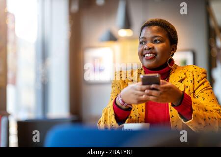 Fröhliche junge Frau mit Smartphone in einem Café Stockfoto