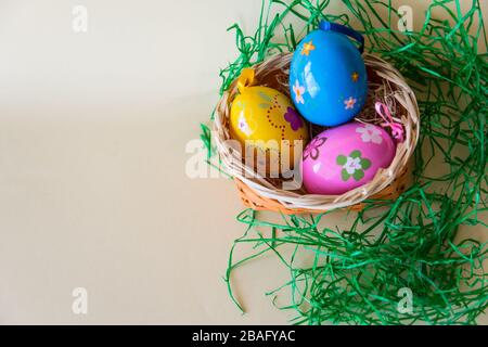 Osterfarbeneier in der Natur Korbkorb auf Pastellgrund. Flaches Lay. Draufsicht mit Kopierbereich. Osterkonzept. Stockfoto