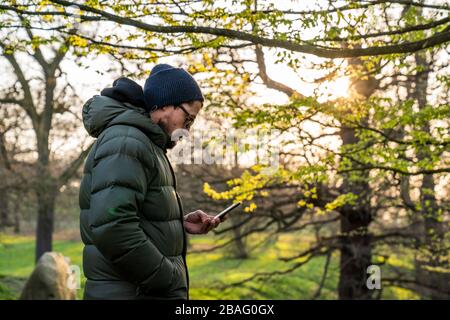 Sport im Greenwich Park. MID 40er-Mann mit Blick auf das Telefon. Stockfoto