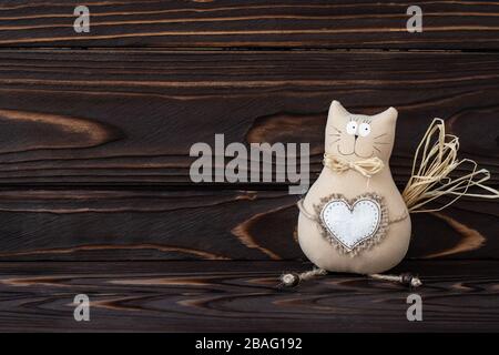 Heimwerker, Katzen-Spielzeug auf Holzhintergrund. Handgemacht Kitty mit Herz aus Textil. Dunkles Holz Naturbretter, Textraum. Romantische Karte, Liebeskonzept. Jahrgang Stockfoto