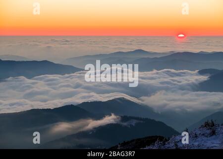 Niedrige Wolken im Bergtal und bunter Sonnenaufgang vom Berggipfel im Winter, den rumänischen Karpaten. Stockfoto