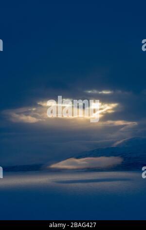 Blick vom Hotel Fjallet mit dramatischem Licht und Wolken über dem gefrorenen und schneebedeckten Tornetrasksee im schwedischen Lappland, Nordschweden. Stockfoto