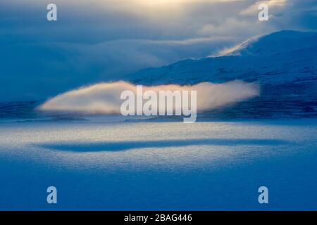 Blick vom Hotel Fjallet mit dramatischem Licht und Wolken über dem gefrorenen und schneebedeckten Tornetrasksee im schwedischen Lappland, Nordschweden. Stockfoto