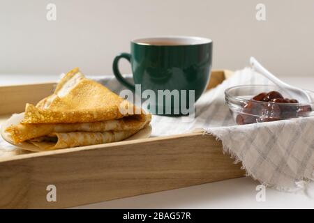 Pfannkuchen (Russisch Blini) mit Erdbeermarmelade und Tee auf einem Tablett Frühstück. Сlose auf. Stockfoto