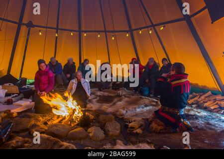 Touristen in einem Lavvu, einem Zelt, das eine temporäre Wohnung ist, die von den samischen Leuten hier im samischen Dorf Ravttas bei Kiruna im schwedischen Lapla benutzt wird Stockfoto