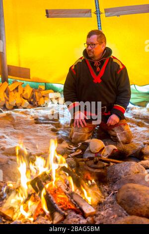 Ein samischer Mann sitzt am Feuer in einem Lavvu, einem Zelt, das eine temporäre Wohnung ist, die von den samischen Leuten hier im samischen Dorf Ravttas nea benutzt wird Stockfoto