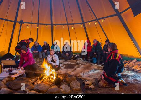 Touristen in einem Lavvu, einem Zelt, das eine temporäre Wohnung ist, die von den samischen Leuten hier im samischen Dorf Ravttas bei Kiruna im schwedischen Lapla benutzt wird Stockfoto