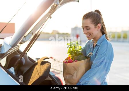 Junge Frau auf dem Parkplatz, die Einkaufen in den Kofferraum des Autos lädt Stockfoto