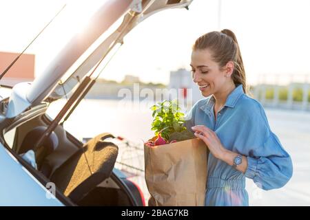Junge Frau auf dem Parkplatz, die Einkaufen in den Kofferraum des Autos lädt Stockfoto