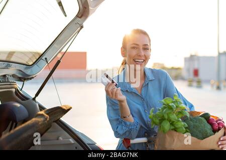 Junge Frau auf dem Parkplatz, die Einkaufen in den Kofferraum des Autos lädt Stockfoto
