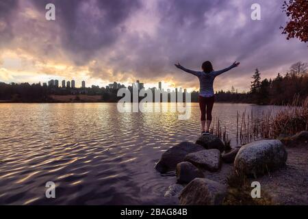 Burnaby, Greater Vancouver, British Columbia, Kanada. Mädchen, die während eines bunten und lebendigen Winteruntergangs mit M die schöne Aussicht auf den Deer Lake beobachten Stockfoto