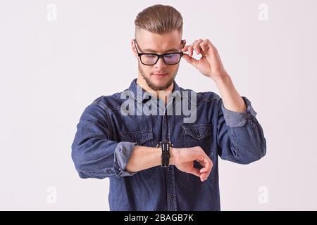 Portrait junger gutaussehender Mann, der Brille trägt und die Uhr vor weißem Hintergrund auf der Hand betrachtet. Attraktiver Flusspferd in Denim s Stockfoto