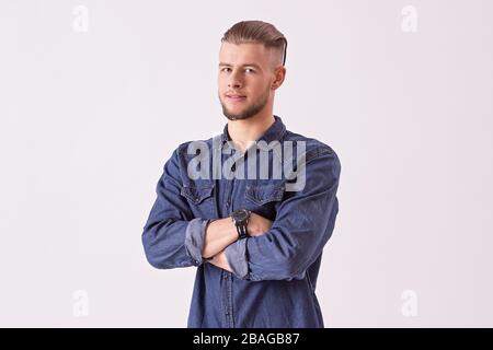 Porträt eines hübschen Hüftmänners, der die Arme überfahren und zur Kamera schaut, während er vor weißem Hintergrund steht. Erfolgreicher Geschäftsmann in Denim s. Stockfoto