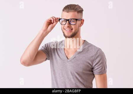 Studio von charmantem jungen Mann in T-Shirt mit Brille und lächelnd, isoliert auf weißem Hintergrund. Charismatischer und stilvoller bärtiger Hüpfer Stockfoto